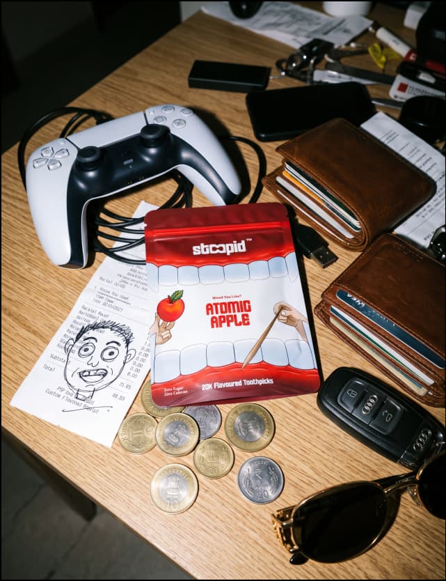 Stoopid Atomic Apple pouch on a desk with PS5 controller, wallet, coins, and keys